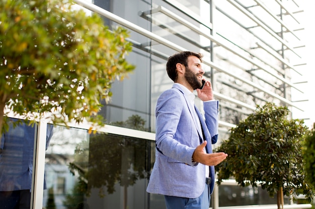 Jeune homme avec un téléphone mobile par un immeuble de bureaux