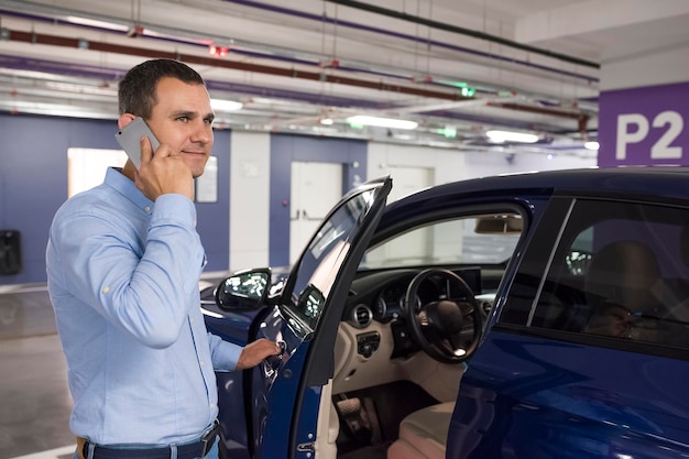 Jeune homme avec téléphone ouvrant la porte de la voiture bleue