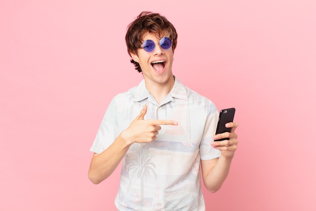 Jeune homme avec un téléphone portable à excité et surpris en pointant sur le côté