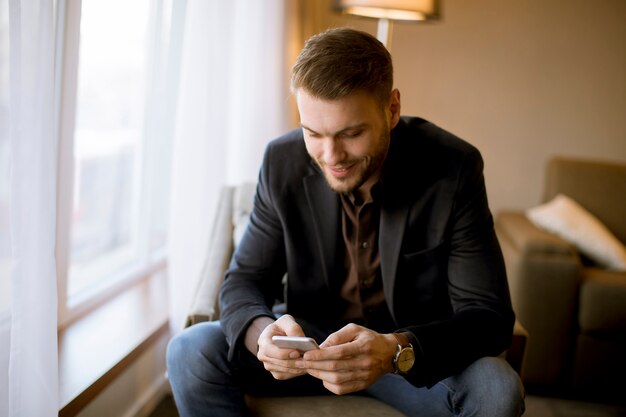 Jeune homme avec un téléphone portable par la fenêtre