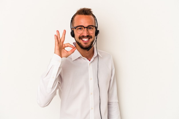 Jeune homme télévendeur caucasien avec des tatouages isolés sur fond blanc joyeux et confiant montrant un geste ok.