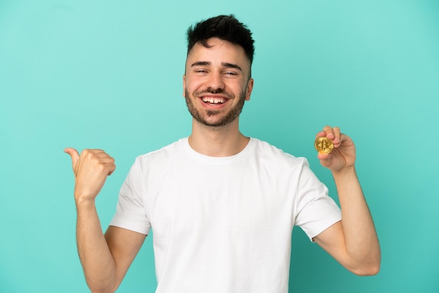 Jeune homme tenant un Bitcoin isolé sur fond bleu pointant vers le côté pour présenter un produit