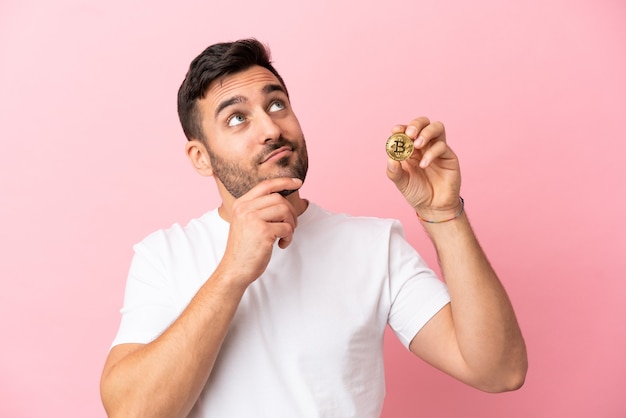 Jeune homme tenant un Bitcoin isolé sur fond rose et levant