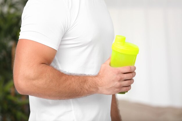 Jeune homme tenant une bouteille avec shake protéiné sur fond flou