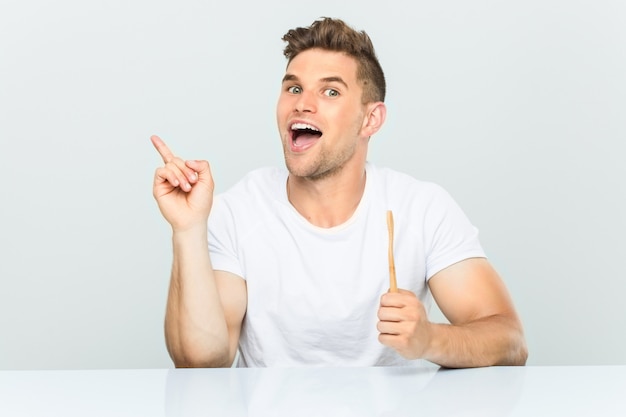 Jeune homme tenant une brosse à dents souriant joyeusement pointant avec l'index loin.