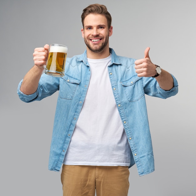 Jeune homme tenant une chemise de jeans tenant un verre de bière debout sur un mur gris.