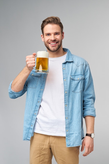 Jeune homme tenant une chemise de jeans tenant un verre de bière debout sur un mur gris.