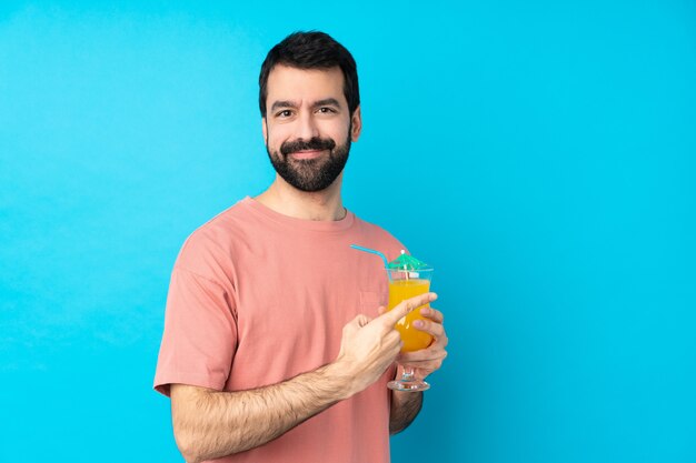 Jeune homme tenant un cocktail sur un mur bleu isolé pointant vers le côté pour présenter un produit