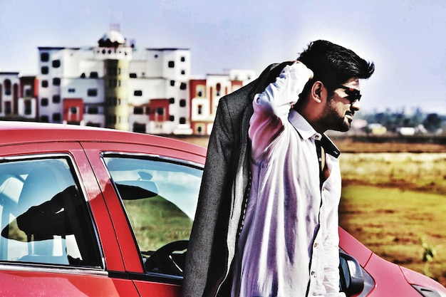 Photo jeune homme tenant un costume debout près de la voiture contre le ciel