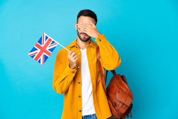 Jeune homme tenant un drapeau du Royaume-Uni isolé sur un mur jaune couvrant les yeux par les mains. Je ne veux pas voir quelque chose