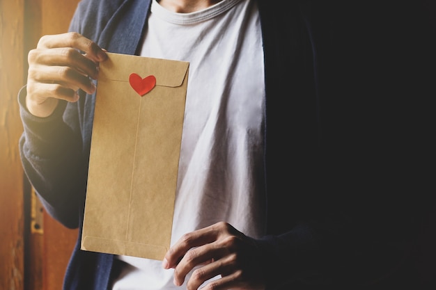 Jeune homme tenant une enveloppe brune décorée d'un coeur de symbole