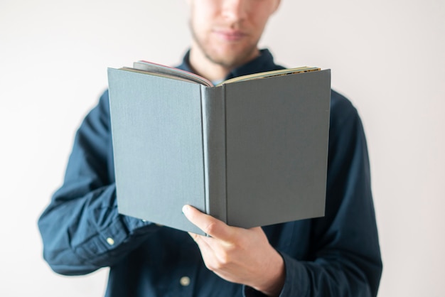 Un jeune homme tenant un livre, lisant et apprenant debout près du mur, isolé