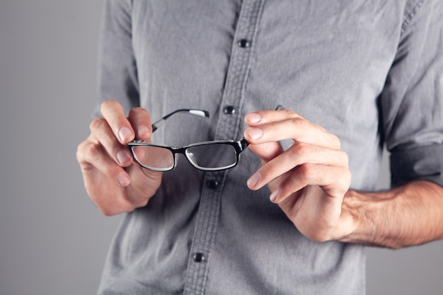 Jeune homme tenant des lunettes optiques sur fond gris