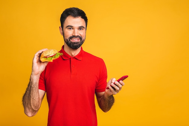 Jeune homme tenant un morceau de sandwich. L'élève mange de la restauration rapide. Le hamburger n'est pas une nourriture utile.