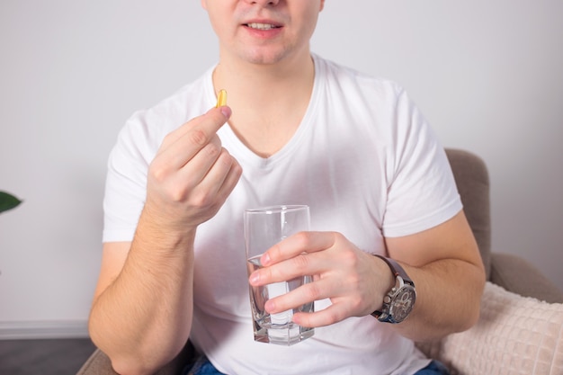 Jeune homme tenant une pilule dans une capsule et un verre d'eau.