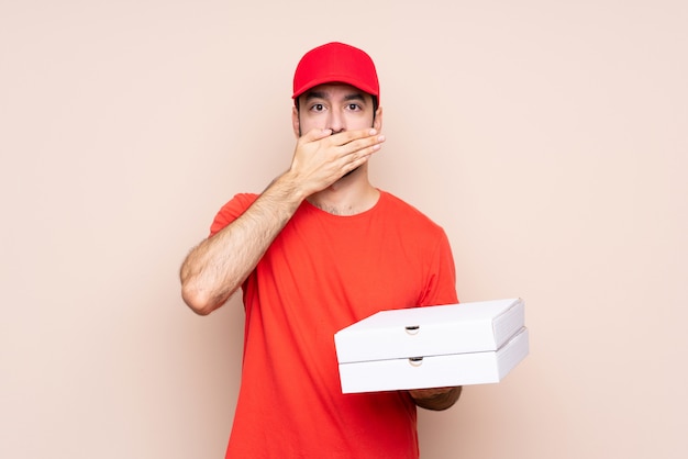 Jeune homme tenant une pizza sur fond isolé couvrant la bouche avec les mains