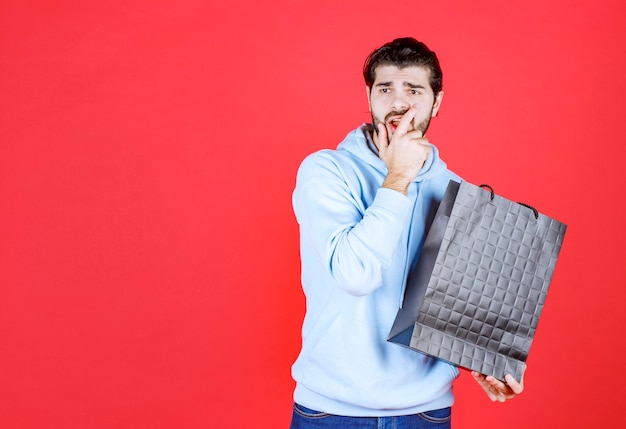 Jeune homme tenant son sac et regardant loin sur le mur rouge