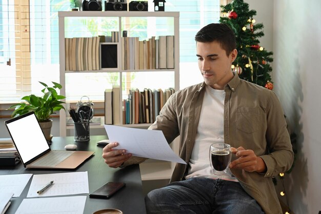 Jeune homme tenant une tasse de café et lisant un document