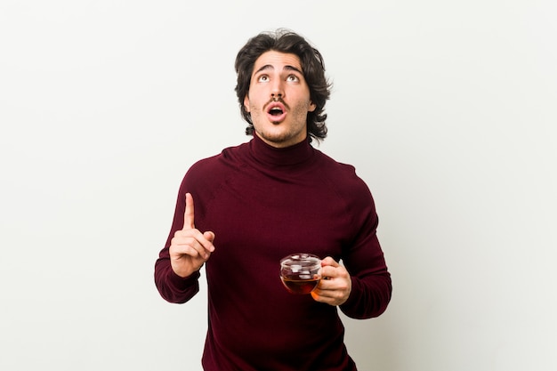 Jeune homme tenant une tasse de thé pointant à l'envers avec la bouche ouverte.