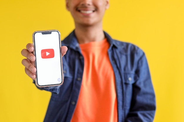 Un jeune homme tenant un téléphone portable avec le logo YouTube sur l'écran isolé sur un fond jaune