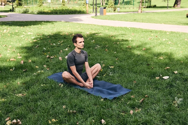 Jeune homme en tenue de sport, faire du yoga dans le parc