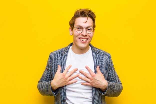 Jeune homme à la tête rouge à l'air heureux, surpris, fier et excité, pointant vers soi contre l'orange