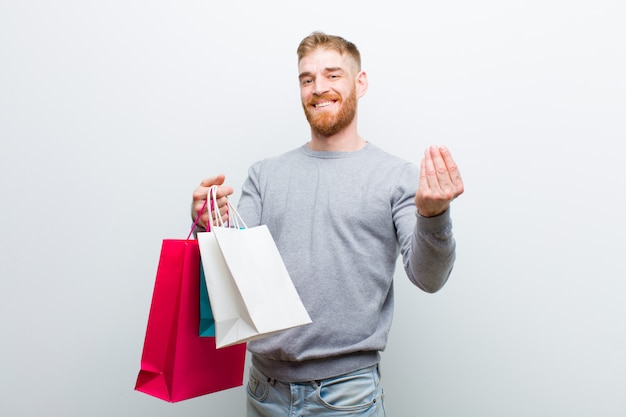 Jeune homme à la tête rouge avec des sacs à provisions contre blanc