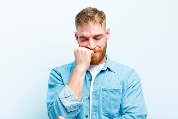 Jeune homme à tête rouge se sentant sérieux, réfléchi et inquiet, regardant de côté avec la main pressée contre le menton