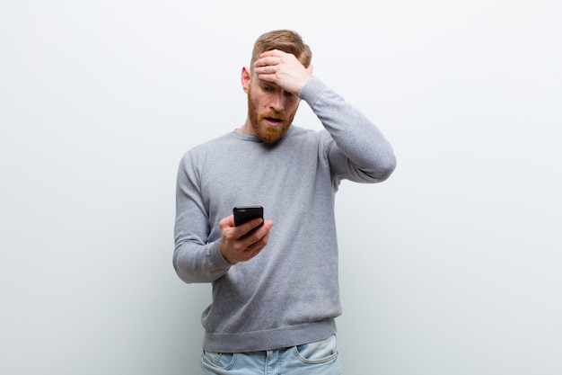 Jeune homme tête rouge avec un téléphone intelligent sur fond blanc