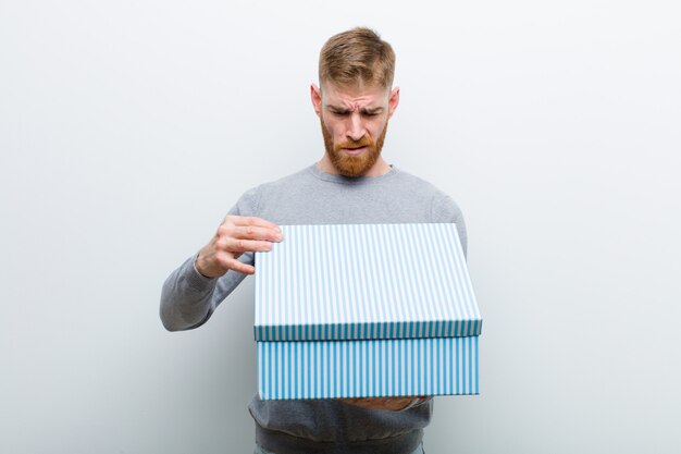 Photo jeune homme à la tête rouge tenant une boîte-cadeau sur fond blanc