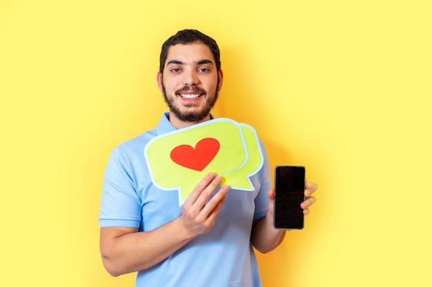 Jeune homme tient une bulle avec un cœur et montre l'écran vide du téléphone intelligent Concept de médias sociaux