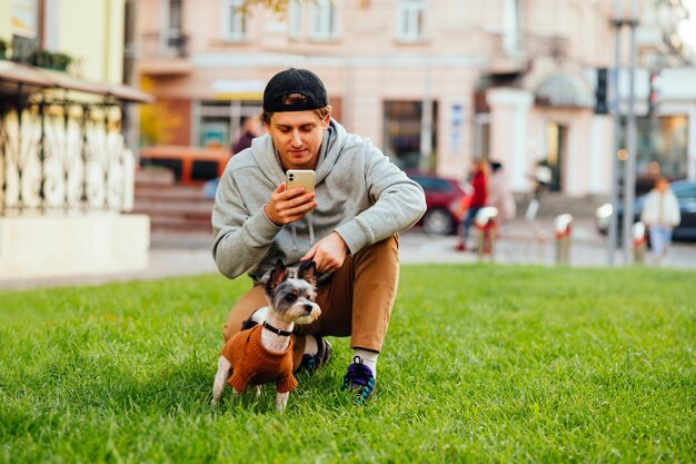 Jeune homme tient un chien en laisse et utilise un smartphone sur la pelouse dans la rue