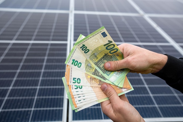 Un jeune homme tient dans ses mains une somme ronde de billets en euros pour l'installation de panneaux solaires Concept d'électricité verte économique