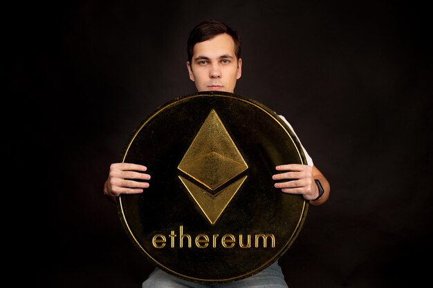 Un jeune homme tient un symbole de la pièce de monnaie ethereum, une monnaie moderne pour l'échange et les achats