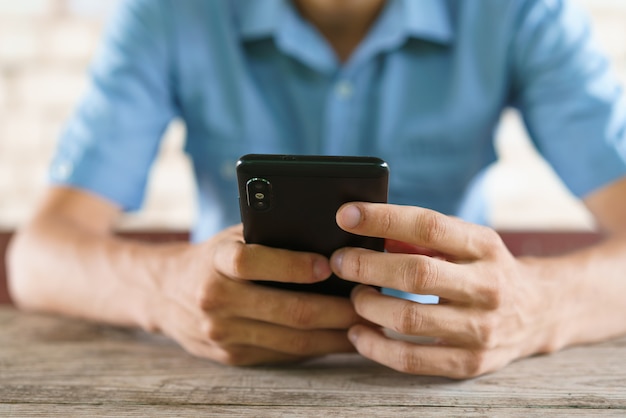 Le jeune homme tient le téléphone dans ses mains et envoie un texto à un gars assis à la table en train de jouer à des jeux en ligne.