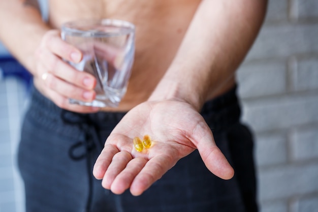 Un jeune homme tient des vitamines et un verre d'eau dans ses mains. Pilules d'immunité