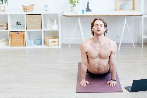 Jeune homme torse nu faisant des exercices d'étirement sur un tapis d'exercice dans le salon à la maison