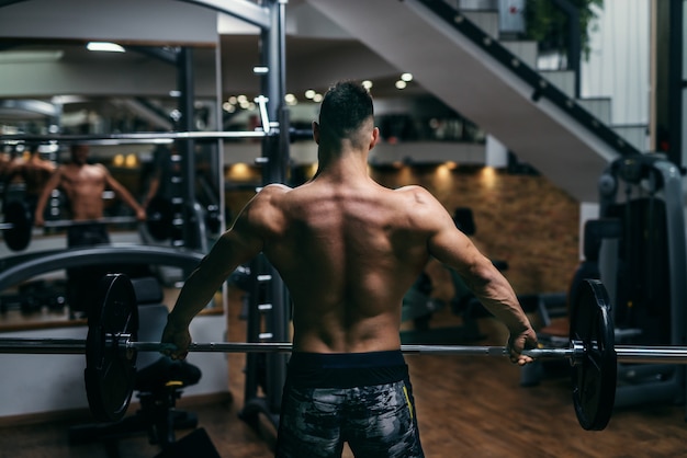 Jeune homme torse nu musclé fort soulevant des haltères avec le dos tourné