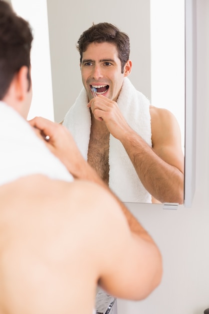 Jeune homme torse nu avec réflexion se brosser les dents