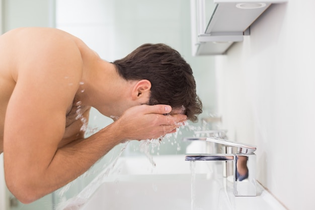 Jeune homme torse nu, se laver le visage dans la salle de bain