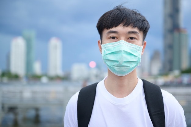 Un jeune homme touriste asiatique porte un masque de protection debout à l'extérieur, protection contre le coronavirus, nouveau concept de voyage normal