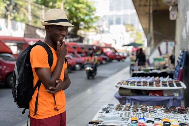 Jeune homme touriste heureux souriant tout en pensant et en choisissant lequel acheter dans les rues de Bangkok en Thaïlande