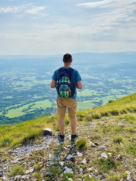 Jeune homme, touriste avec sac bénéficie d'une vue sur le village dans les collines verdoyantes. Ciel bleu. Randonnée. Campagne