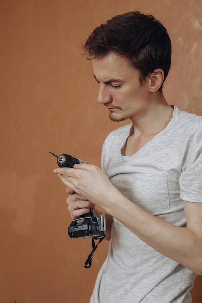 Jeune homme avec un tournevis électrique moderne debout dans la chambre sur fond marron