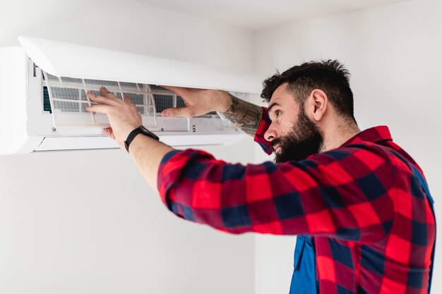 Jeune homme à tout faire barbu réparant le climatiseur.