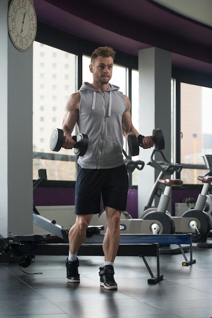 Jeune homme travaillant sur les biceps dans les boucles de concentration d'haltères de gym