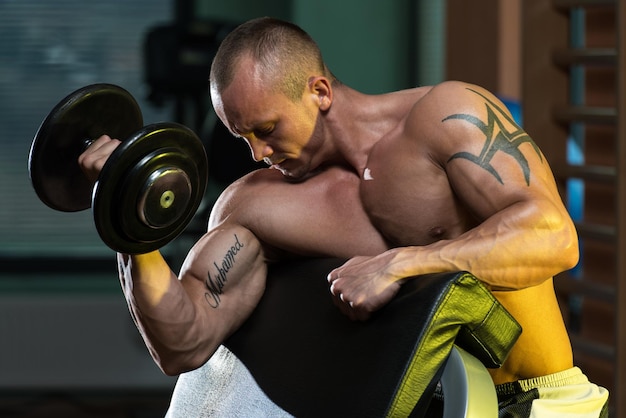 Jeune homme travaillant sur les boucles de concentration d'haltères biceps