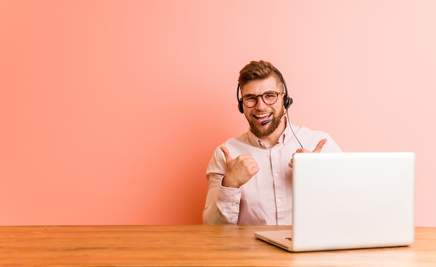 Jeune homme travaillant dans un centre d&#39;appels, levant les deux pouces, souriant et confiant.