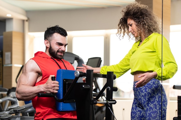 Jeune homme travaillant dans une salle de sport faisant de l'exercice sur la machine avec l'aide de son entraîneur