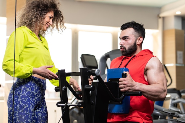 Jeune homme travaillant dans une salle de sport faisant de l'exercice sur la machine avec l'aide de son entraîneur